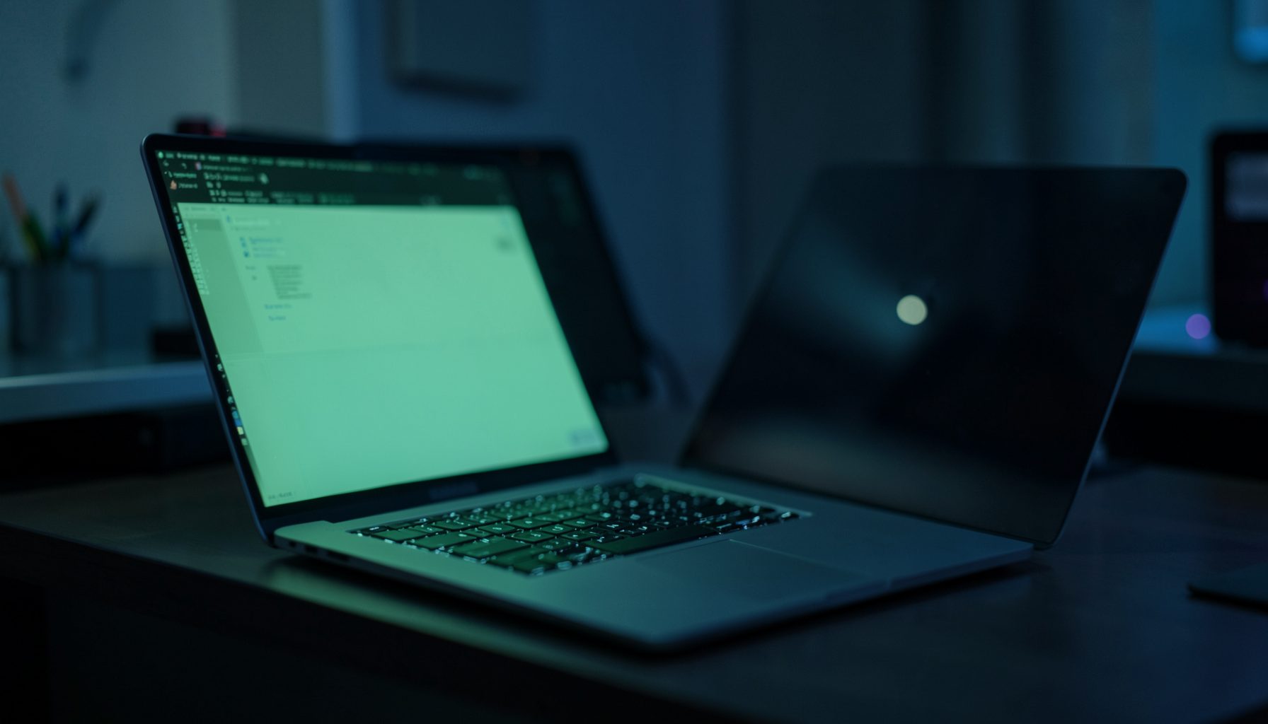 A calm workspace scene with a laptop glowing softly in muted green and dark blue tones, conveying a focused technology atmosphere