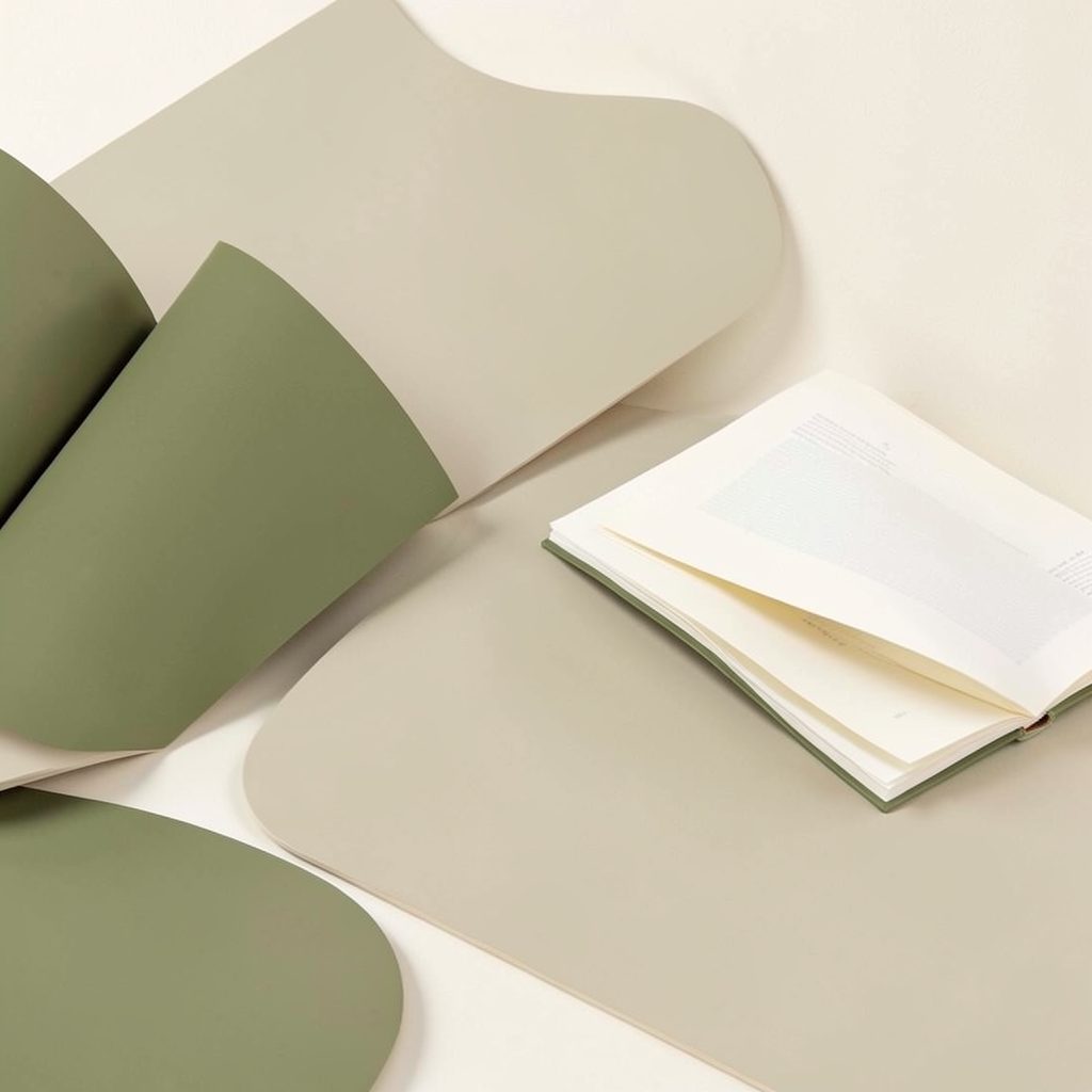 Soft abstract shapes in muted olive and cream tones, suggesting open books and layered pages in a calm, airy composition